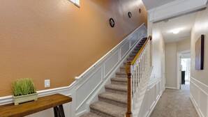 A carpeted staircase with white railings and a wooden handrail, leading to a landing with a small table and a potted plant. - Vista Cay Resort, Next To Universal 821 3 Bedroom Townhouse (Orlando)