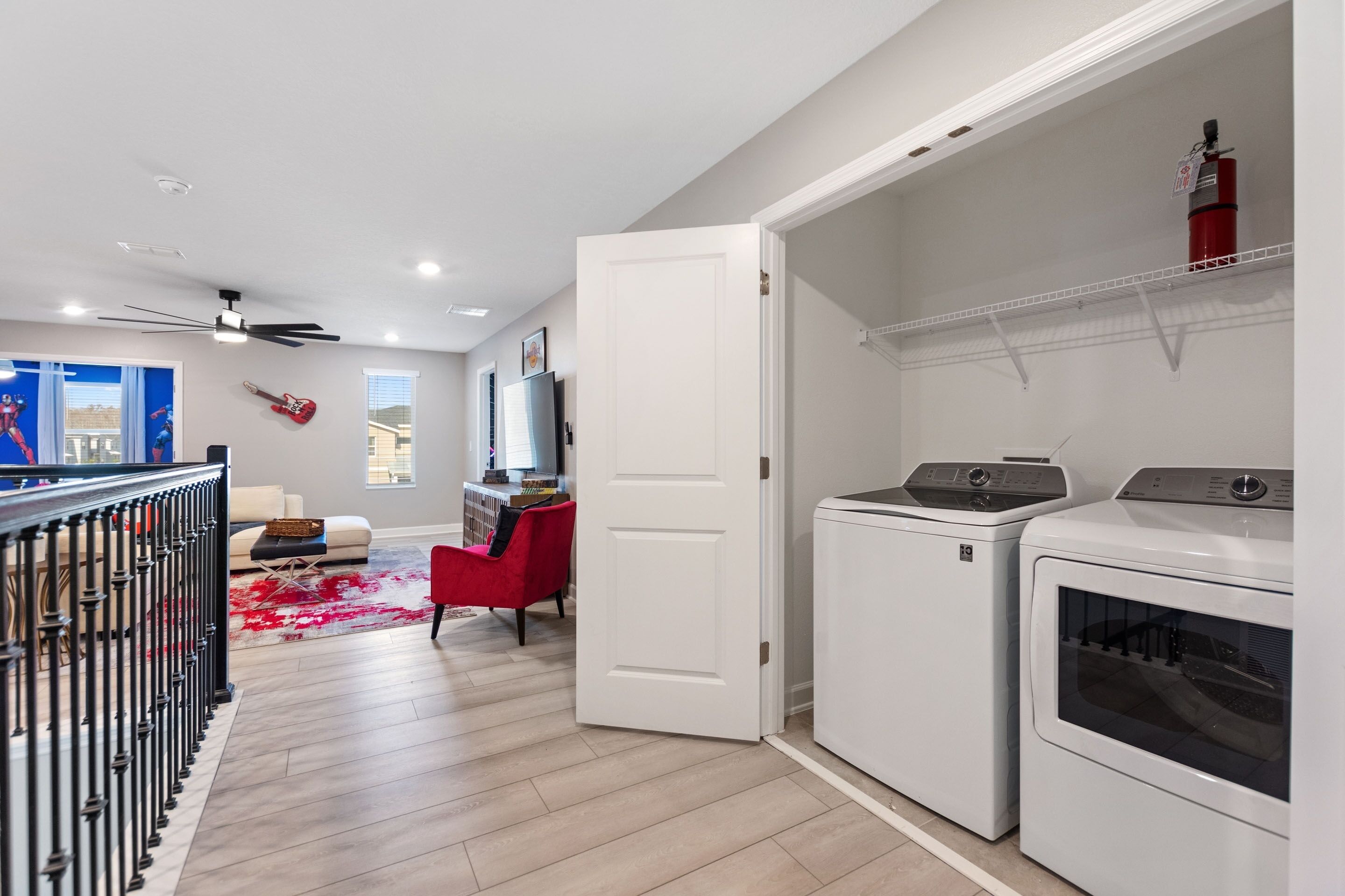 A modern laundry room with a white door, two stacked washing machines, and a ceiling fan.