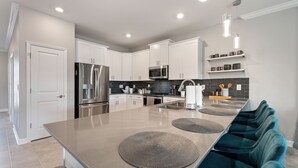Una cocina moderna con armarios blancos, electrodomésticos de acero inoxidable y una isla grande con sillas azul turquesa.