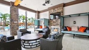 Un espace de détente extérieur avec des meubles en osier, une table ronde, un foyer et une piscine en arrière-plan.