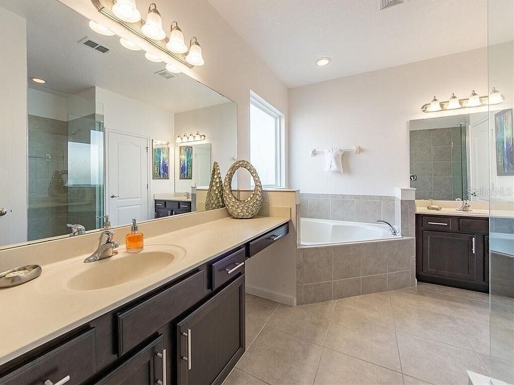A modern bathroom with a large mirror, dual sinks, a bathtub, and a vanity with dark cabinets.