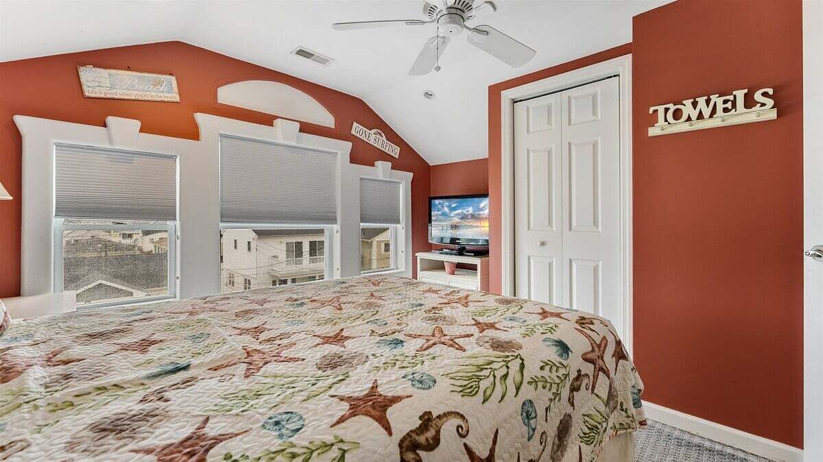 Un dormitorio con cama, televisión, ventilador de techo y un cartel en la pared.