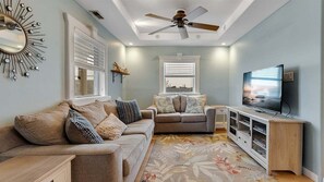 A living room with two sofas, a TV, a ceiling fan, and a decorative mirror.