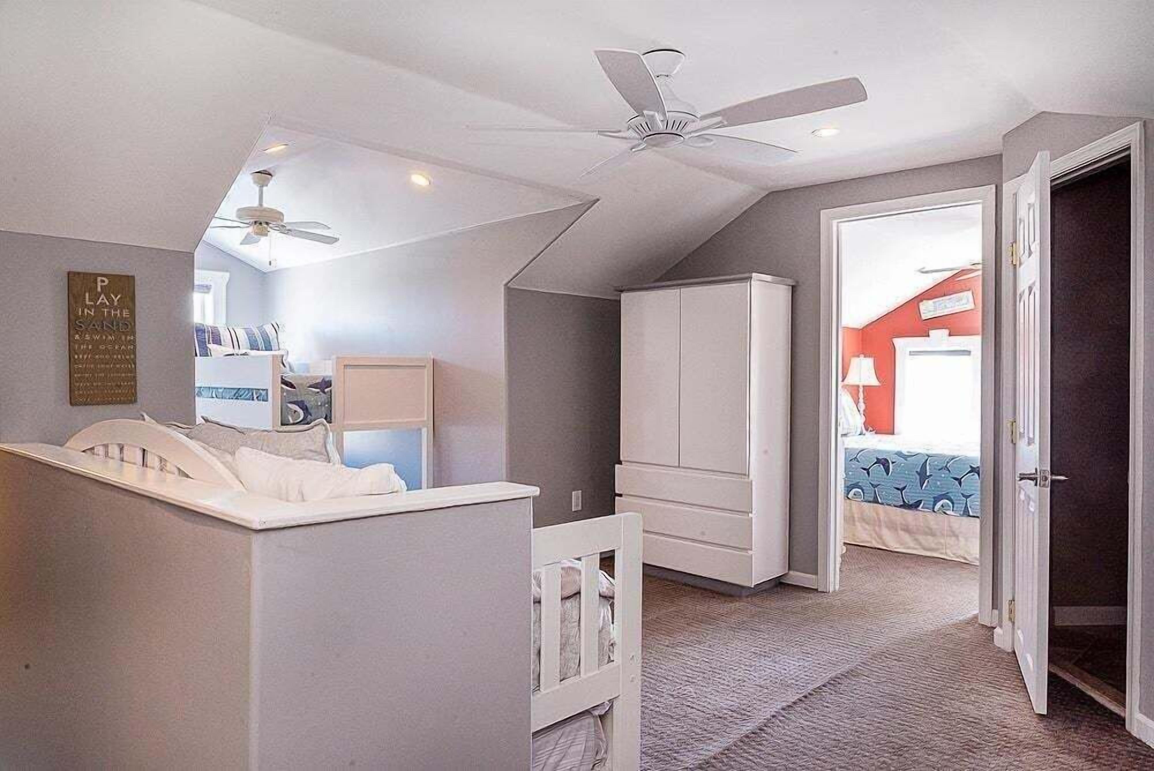 A bedroom with a crib, a wardrobe, a ceiling fan, and a door leading to another room.