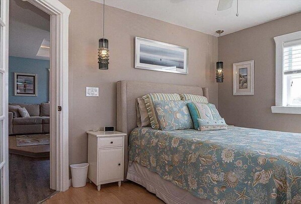 A bedroom with a bed, nightstand, wall art, and a view of another room.