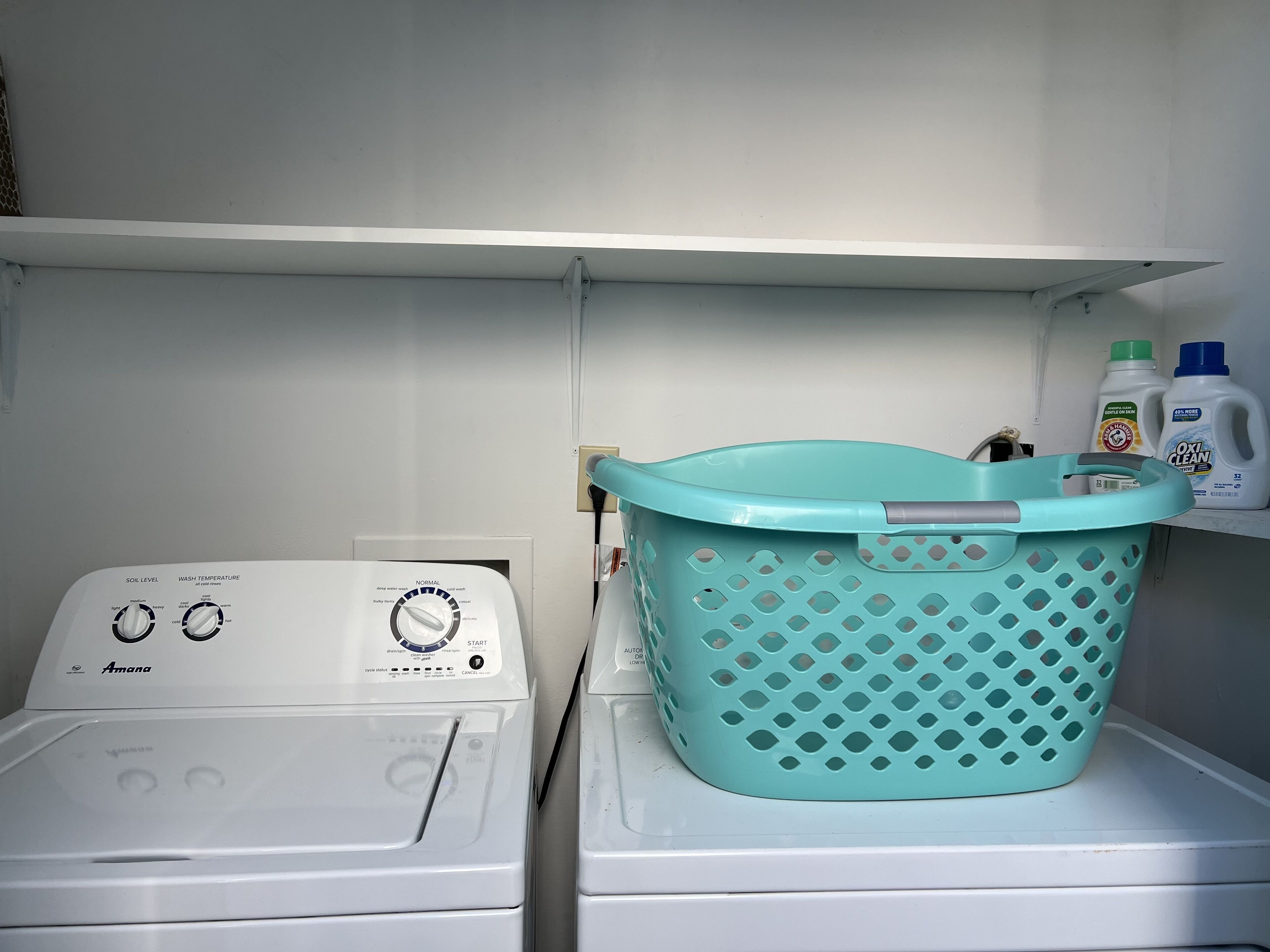 Un espace dédié à la lessive, avec un lave-linge et un panier à linge bleu posé sur une étagère.