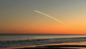 A sunset over the ocean with a visible contrail.