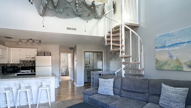 A spacious living area with a gray sofa, a dark ottoman, and a ceiling fan. A spiral staircase leads to an upper level.