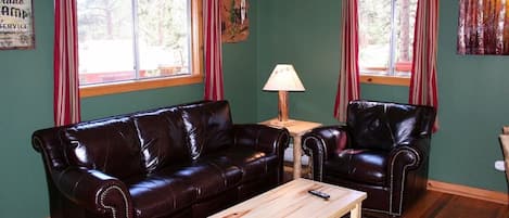 A living room with a dark brown leather sofa, two leather armchairs, a wooden coffee table, and a lamp.