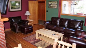 A living room with a brown leather sofa, a wooden coffee table, and a TV mounted on the wall. - Mountain Pine Cabin With Personal Hot Tub - Dog-friendly! 3 Bedroom Cabin - #20-NCD0296 (Estes Park)