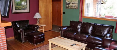 Ein Wohnzimmer mit braunem Ledersofa, einem Holztisch und einem an der Wand befestigten Fernseher.