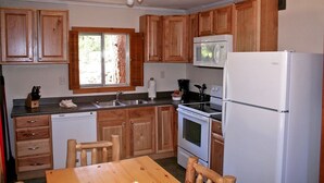 A compact kitchen with wooden cabinets, a white refrigerator, a microwave, an oven, and a dishwasher. - Mountain Pine Cabin With Personal Hot Tub - Dog-friendly! 3 Bedroom Cabin - #20-NCD0296 (Estes Park)