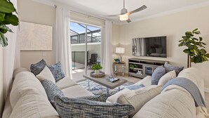 A living room with a sofa set, a coffee table with decorative items, a TV, and a ceiling fan. - Plush Pelican, At Storey Lake By Shine Villas #839 4 Bedroom Home (Kissimmee)