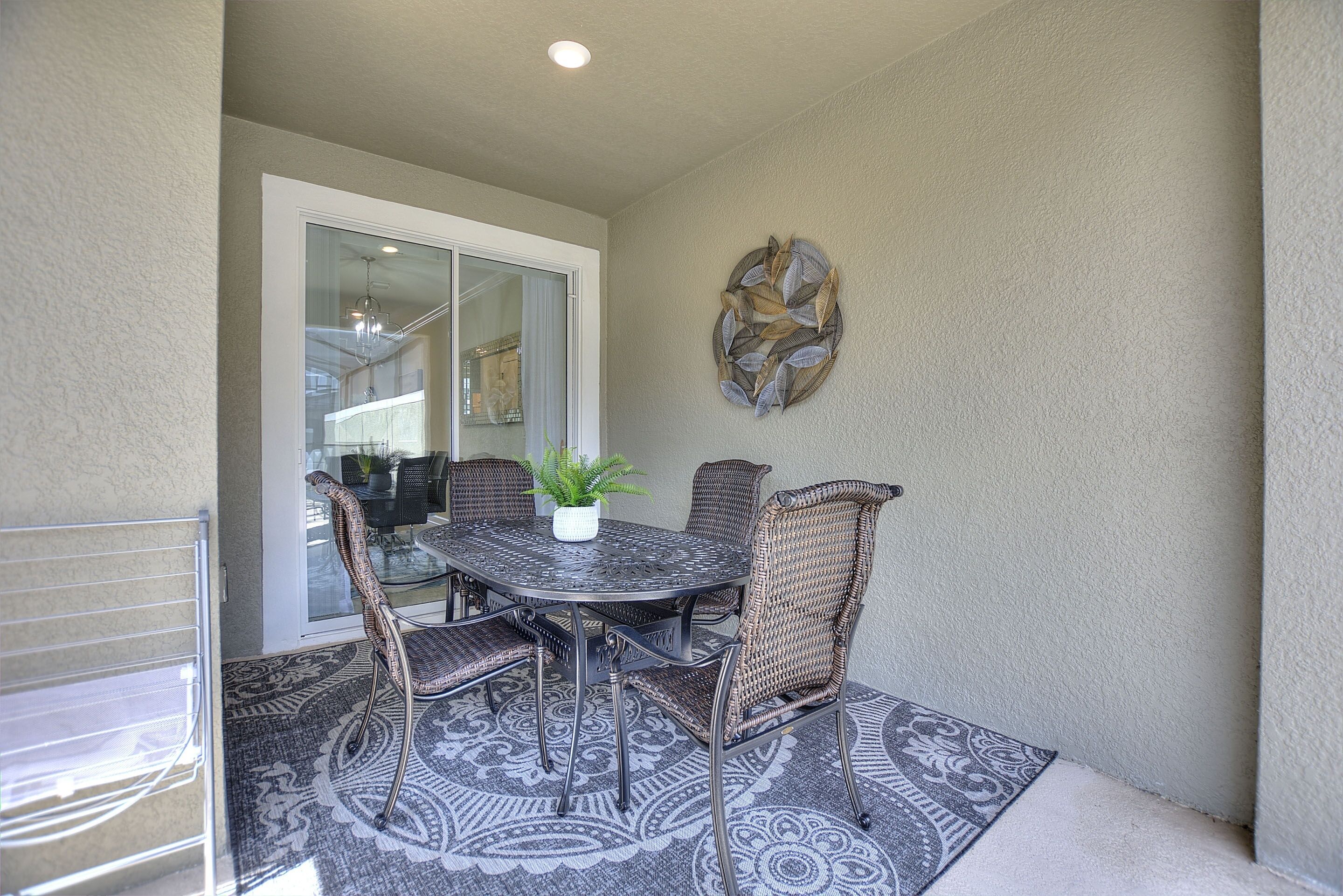 A patio with a round table and four wicker chairs, a potted plant, and a decorative wall piece.