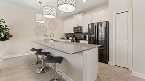 A modern kitchen with a central island, bar stools, stainless steel appliances, and pendant lighting. - Plush Pelican, At Storey Lake By Shine Villas #839 4 Bedroom Home (Kissimmee)
