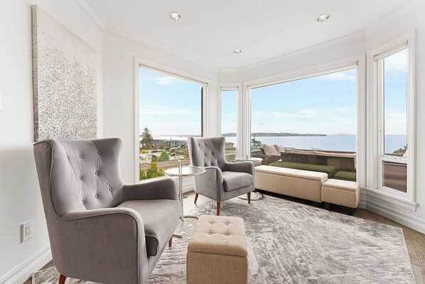 A modern living room with a large window offering a view of a body of water and distant land.