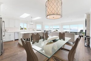 A modern kitchen with white cabinetry, a glass dining table, and a large island.