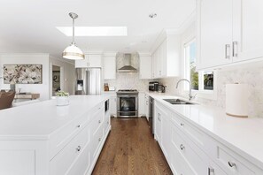 A modern kitchen with white cabinetry, a central island, stainless steel appliances, and a skylight.