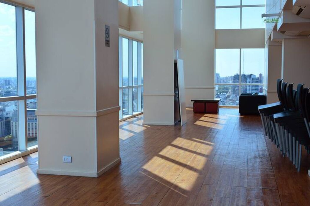 Une pièce spacieuse dotée de grandes fenêtres, d’un plancher en bois et d’un coin salon avec des fauteuils.
