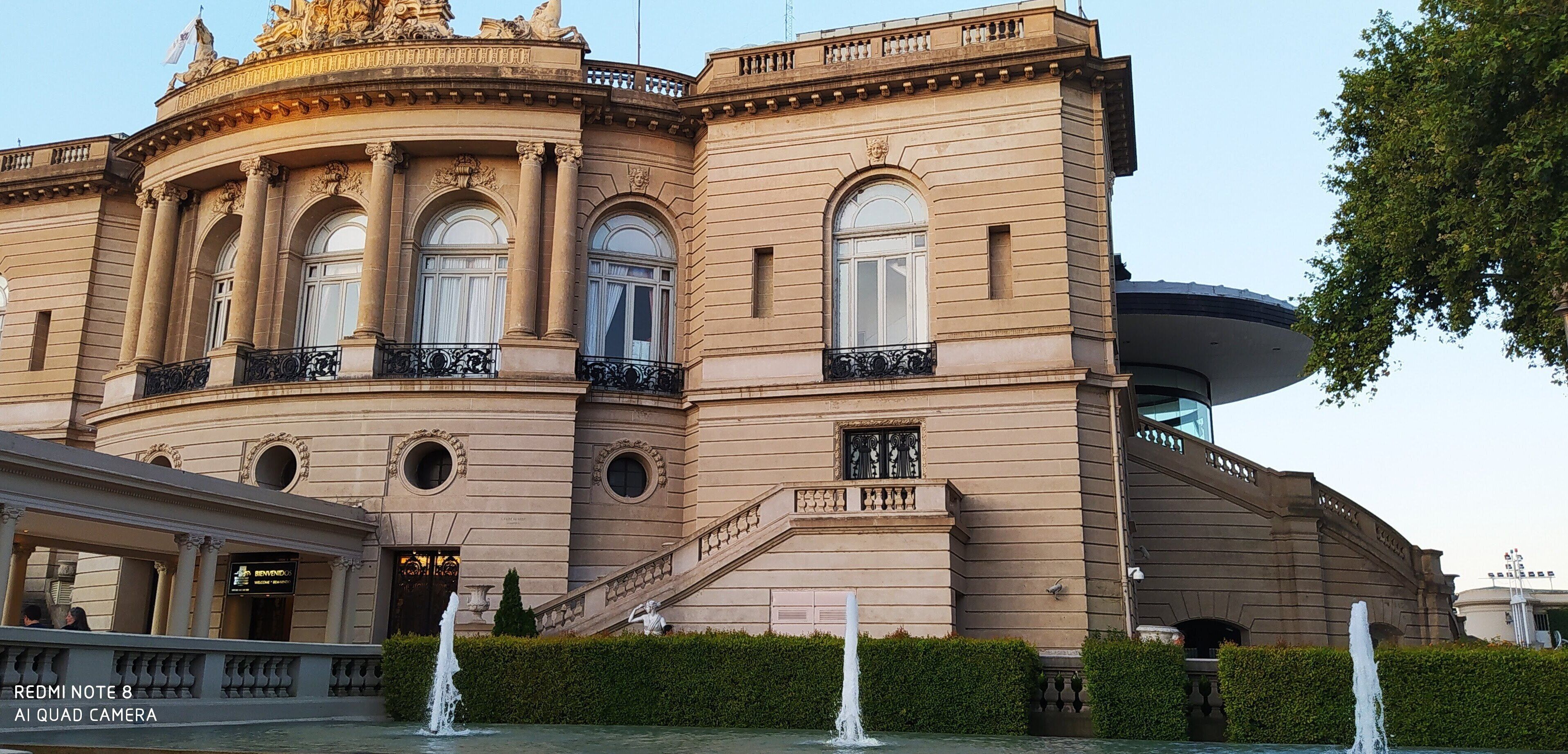 A historic building with classical architecture, featuring a grand entrance, a fountain, and a statue.