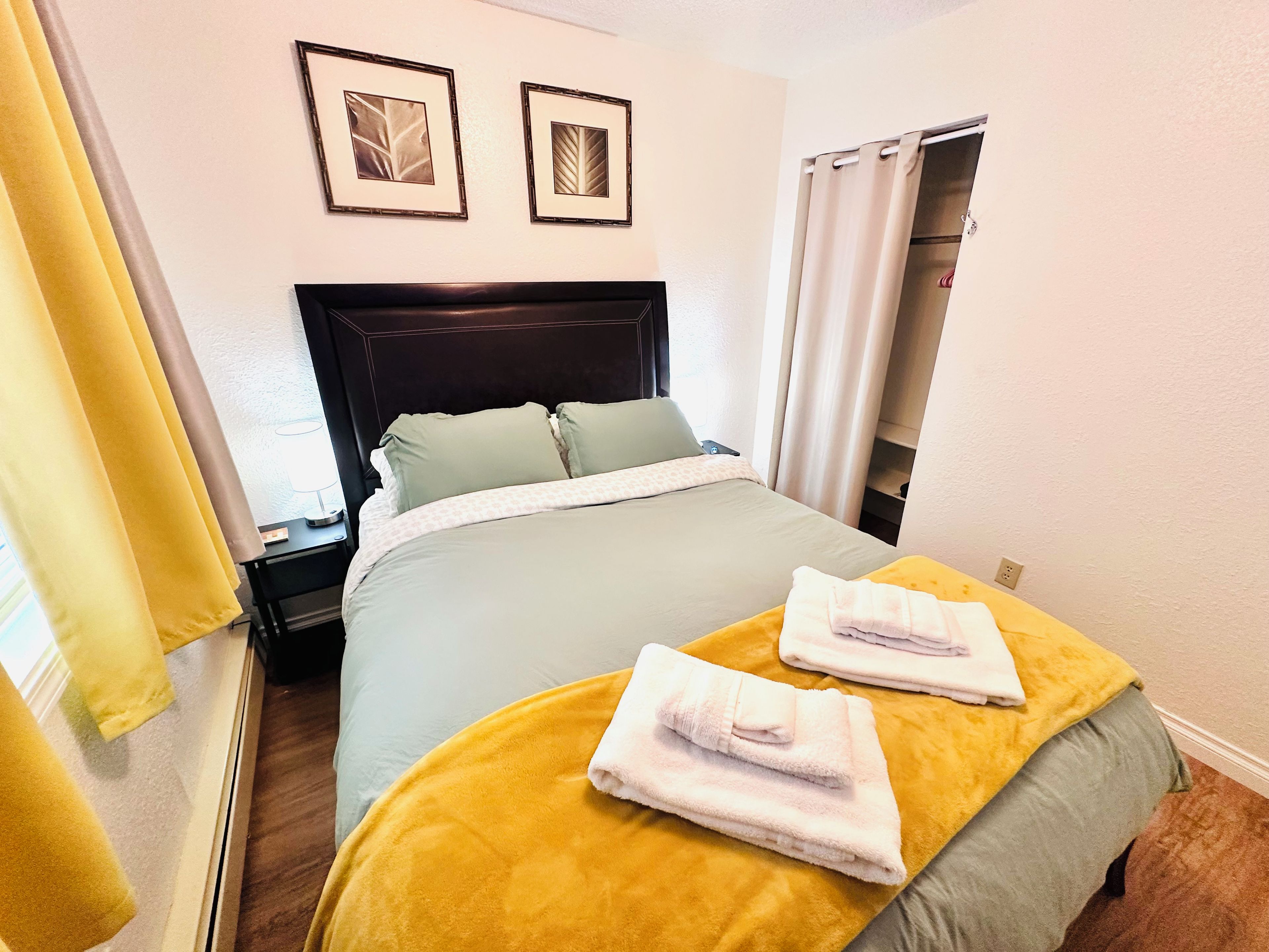 A hotel room with a bed, a nightstand, a wardrobe, and two framed pictures on the wall.