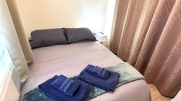 A bed with a pillow, a blanket, and two folded towels.