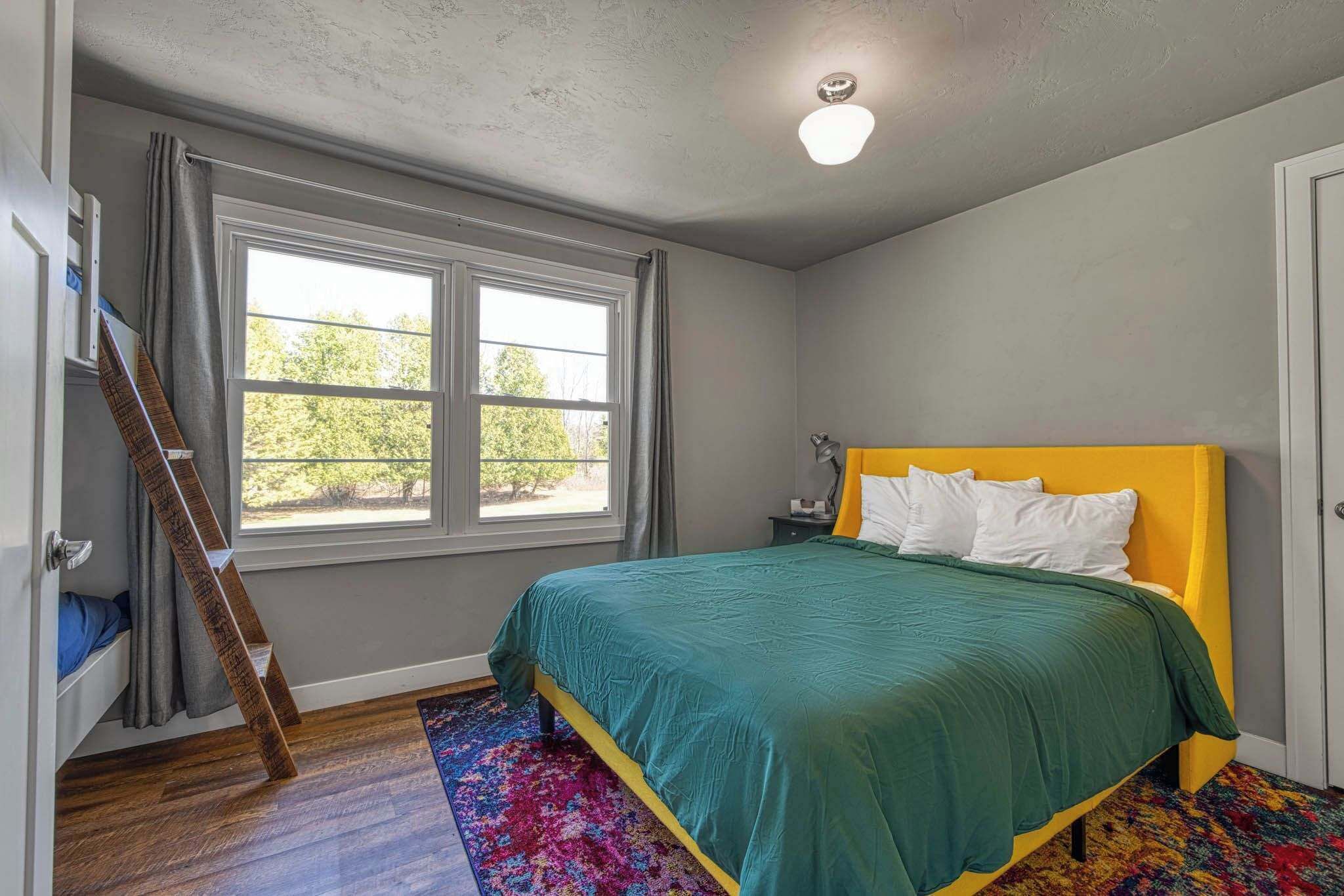 A bedroom with a bed, a window, a ladder, and a colorful rug.