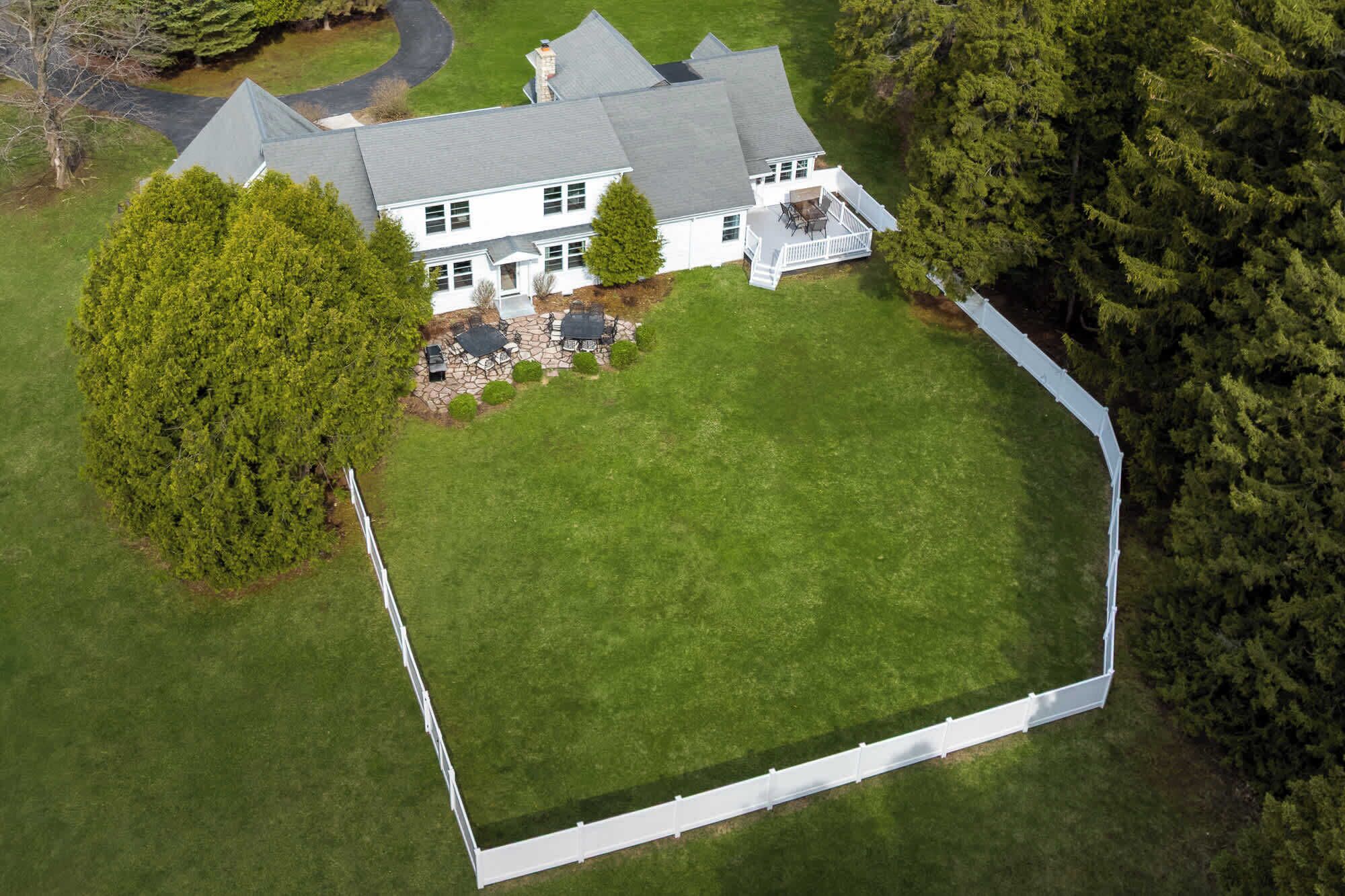 A large house with a spacious lawn, a fenced yard, and a driveway.