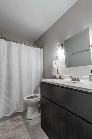 A bathroom with a shower curtain, toilet, vanity with a mirror, and a sink. - Retro home in downtown sister bay-Sleeps 6! (Sister Bay)