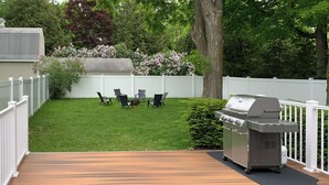 A deck with a grill and chairs in a backyard.