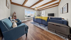 A living room with a blue sofa, a wooden ceiling, a TV, and a large window.
