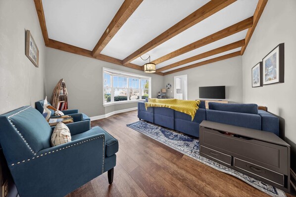 A living room with a blue sofa, a wooden ceiling, a TV, and a large window.