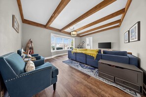 A living room with a blue sofa, a wooden ceiling, a TV, and a large window. - Retro home in downtown sister bay-Sleeps 6! (Sister Bay)