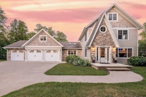 Une maison à deux étages avec une façade en pierre, un garage à trois portes et une pelouse bien entretenue.