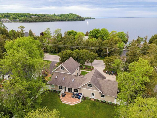 Une maison à deux étages avec une terrasse, entourée d’arbres et offrant une vue sur un lac.