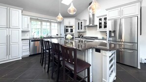 Una cocina moderna con armarios blancos, electrodomésticos de acero inoxidable y una isla central con taburetes de bar.