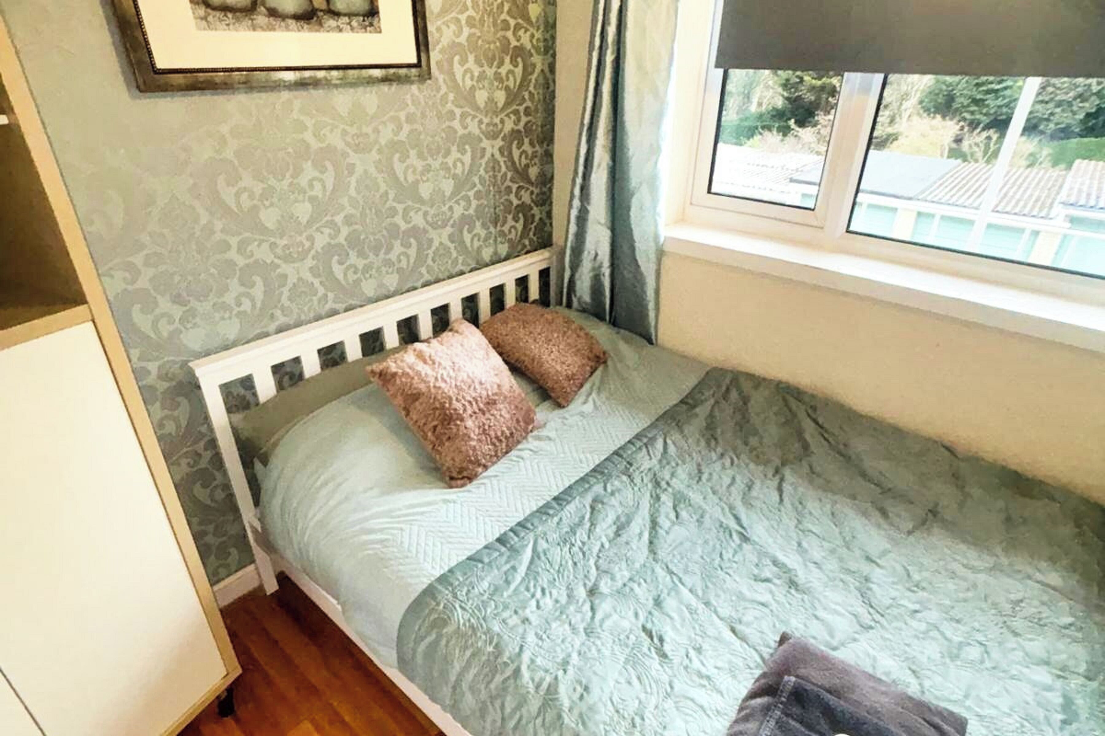 A single bed with a white headboard, two pillows, and a light blue quilt.