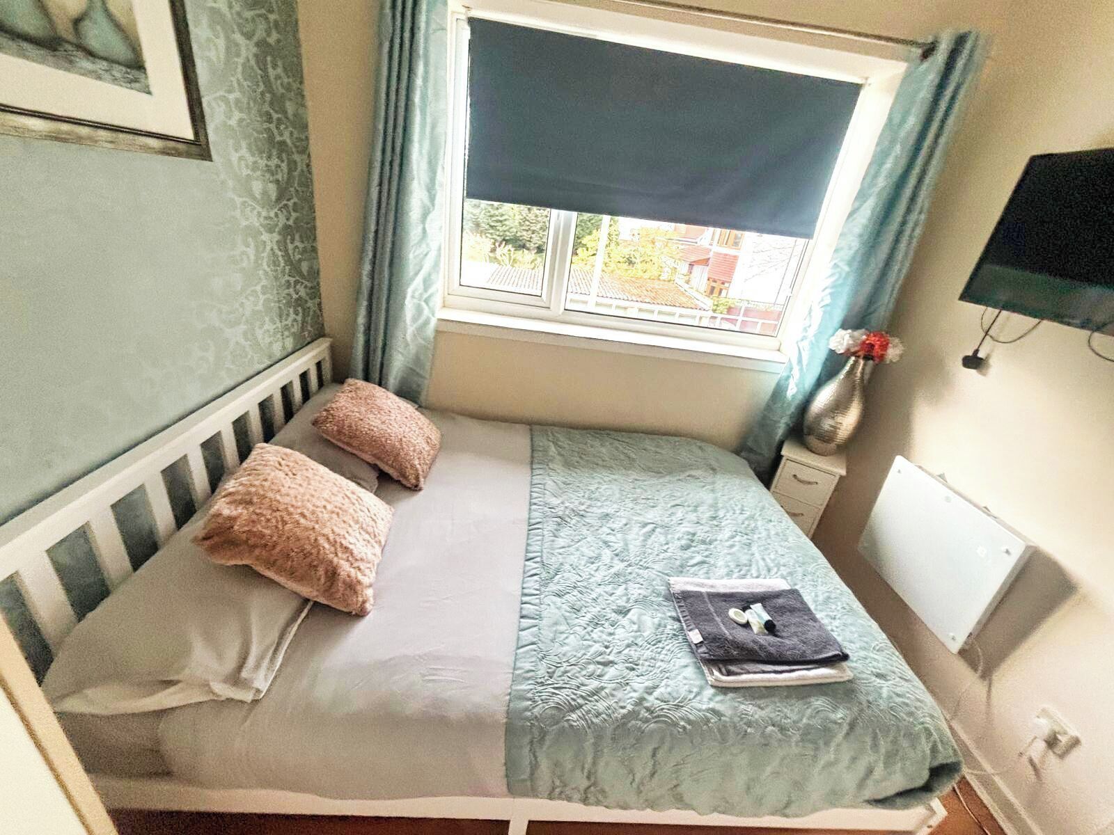 Een klein, netjes opgemaakt bed met een blauw-witte quilt, twee kussens en een opgevouwen handdoek ernaast.