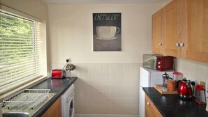Una cuina amb rentadora, torradora vermella, bullidor i cafetera.