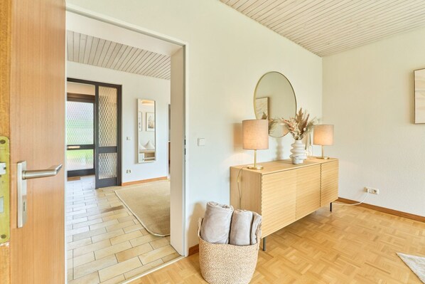 A modern interior with a wooden floor, a wooden console table with a mirror and lamps, and a woven basket with cushions.