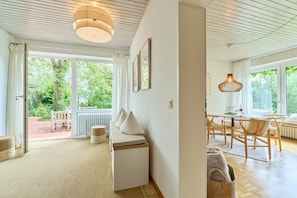 A modern interior with a sofa, dining table, and chairs, large windows, and a ceiling with wooden slats.