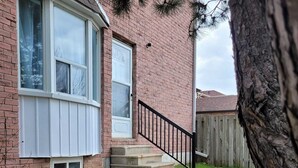 A brick house with a front porch, a small set of concrete steps, and a wooden fence in the background. - Cozy resting place for one (Toronto)