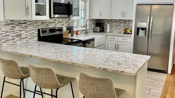 Una cocina moderna con armarios blancos, encimera de granito y refrigerador de acero inoxidable.
