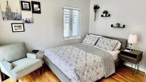 Un dormitorio con cama, una silla, una mesita de noche, ventilador de techo y decoración en la pared.