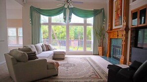 Ein Wohnzimmer mit einer Couch, einem Kamin und einem großen Fenster mit Vorhängen.