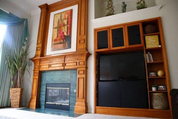 A living room with a fireplace, a large flat-screen TV, wooden shelving with decorative items, and a framed painting above the fireplace. - Perfect place for relaxing in the heart of Murphy (Murphy)