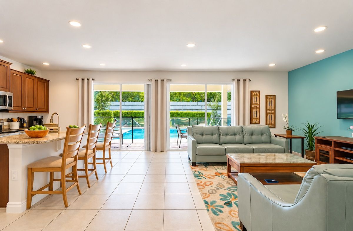 A modern living room with a sofa, coffee table, and a dining area with chairs and a kitchen counter.