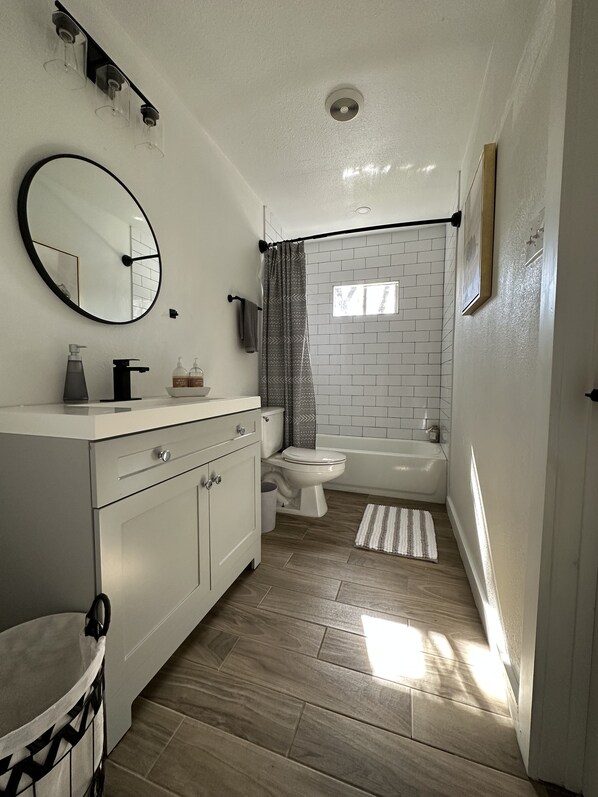 A modern bathroom with a white vanity, a round mirror, a toilet, and a bathtub.