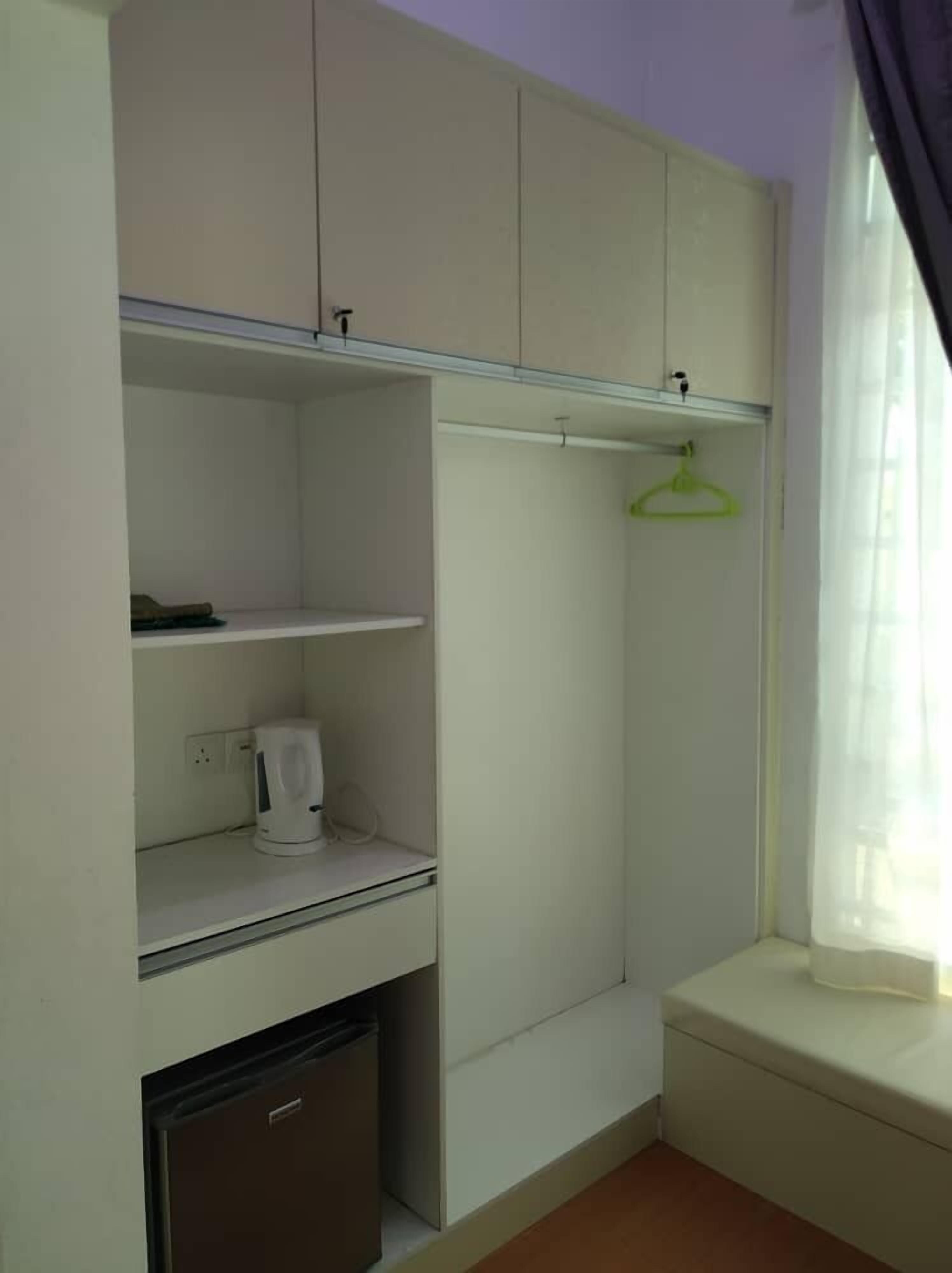 A compact room with a built-in wardrobe, a small kitchenette with a coffee maker, and a window with a curtain.
