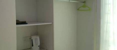 Ein kleines, kompaktes Zimmer mit Einbauschrank, einer Kochnische mit Kaffeemaschine und einem Fenster mit Vorhang.